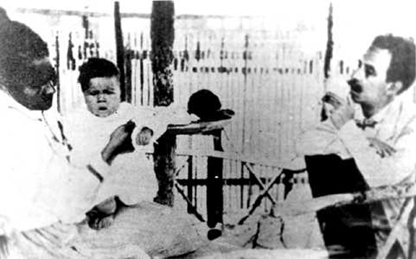 Ao fundo, vê-se o vagão da Estrada de Ferro Central do Brasil, que lhe servia de alojamento e laboratório em Lassance. Por muito tempo pensou-se que tal menina era Berenice, o primeiro caso humano da tripanossomíase americana identificado por Chagas em fevereiro de 1909